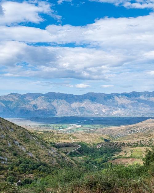 Breathtaking view of the Albanian countryside with mountains and lush valleys under a bright blue sky.