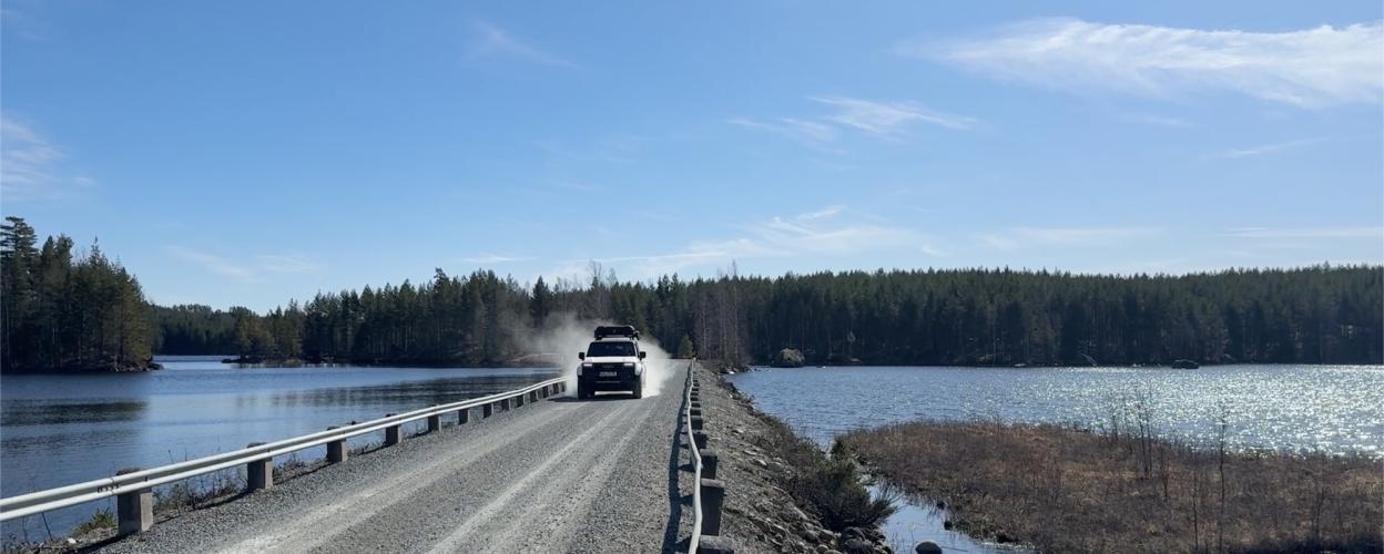 Auto fährt auf einem Schotterweg; link und rechts des Weges ist Wasser 