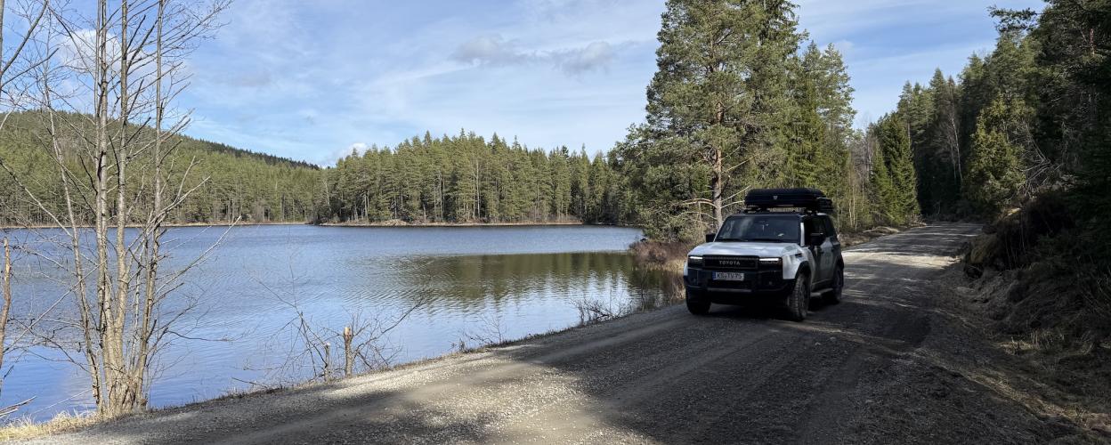 Weißes Offroadauto fährt auf einer breiten Schotterstraße an einem See entlang