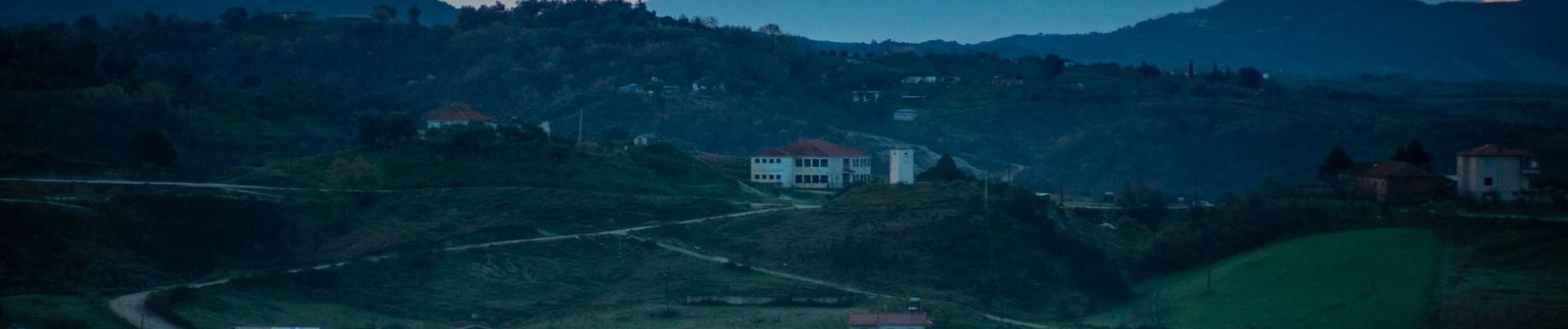 A tranquil rural scene in Albania, showcasing rolling hills and mountains under a sunset sky.