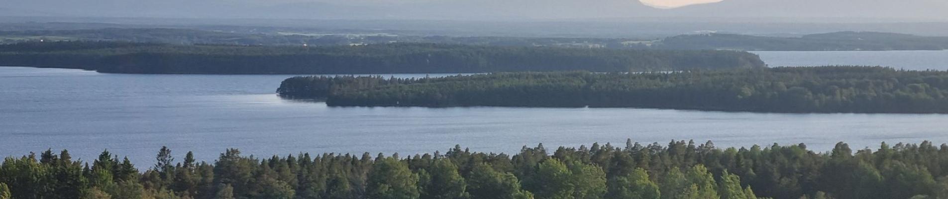 Picturesque landscape featuring a barn, lush forest, and a serene lake under a clear sky.