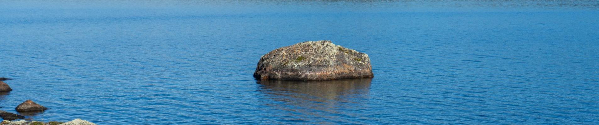 Tranquil lake scene with rocks and forested hills in Norway under a clear sky.