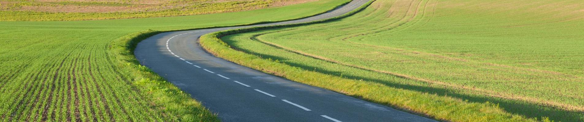 Serene countryside road through green fields in Gommecourt, IDF, France.