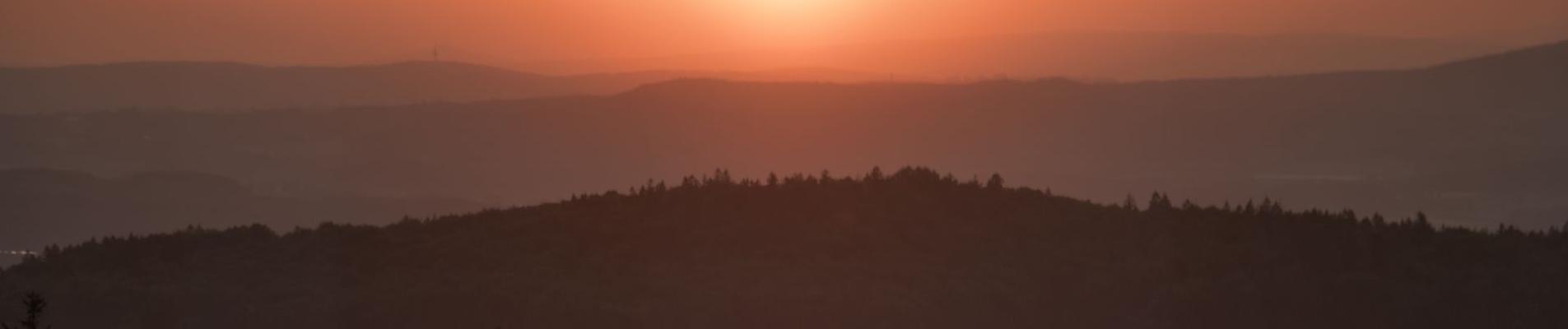 Stunning sunset over Bavarian forest and hills, with vibrant twilight colors.