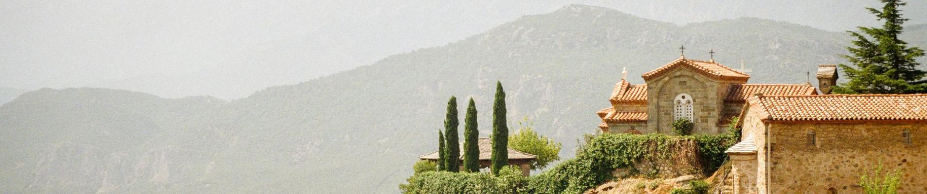 Picturesque monastery perched on a dramatic cliff with mountain backdrop.