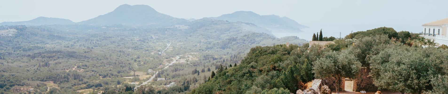 Breathtaking aerial view of Kerkyra's lush landscape with hills, valleys, and ancient structures under a clear sky.