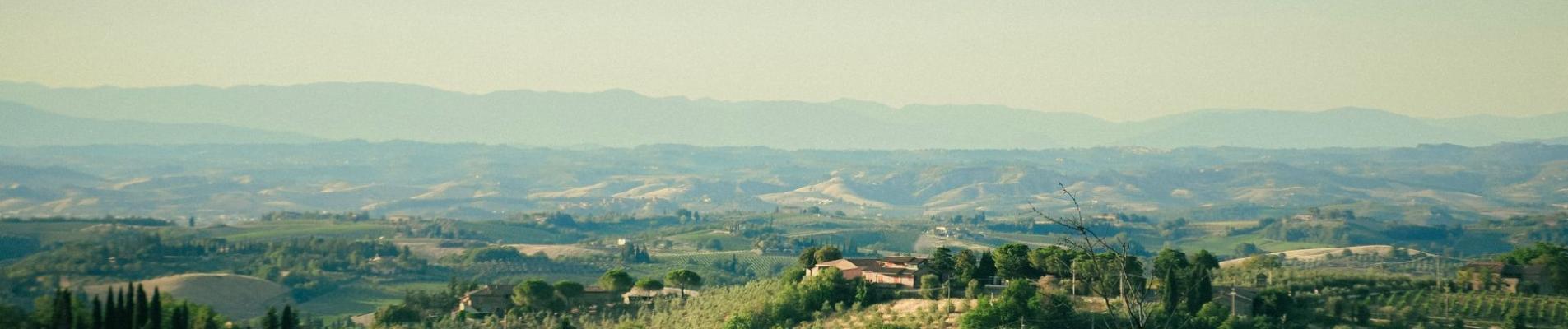 Picturesque view of Tuscany's rolling hills, vineyards, and Italian villas under a clear summer sky.