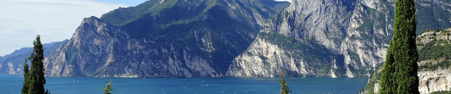 Scenic view of Lake Garda with surrounding mountains and lush green trees in the foreground.