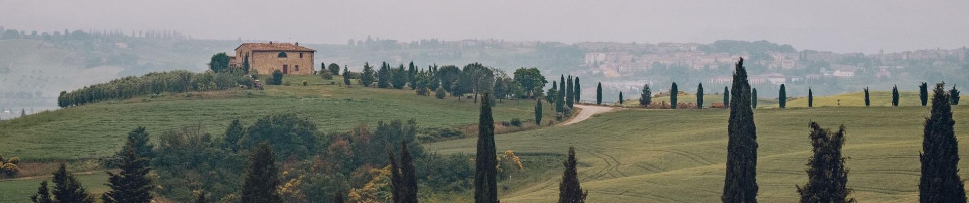 Overcast day in Tuscan hills featuring cypress trees and traditional stone house.