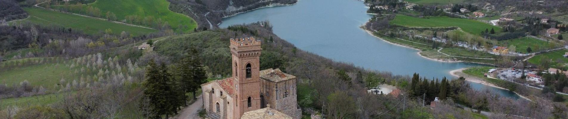 Scenic aerial view of a historic castle on a hill overlooking a beautiful lake and lush valley.