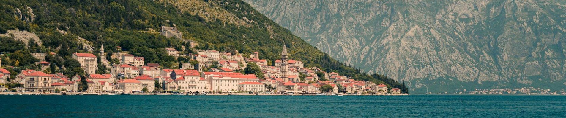 Panoramic view of a coastal town in Montenegro with mountains and sea.