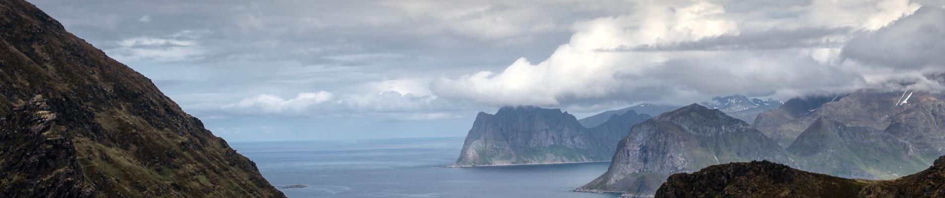 A stunning view of the Lofoten fjord surrounded by rocky mountains and a dramatic cloudy sky.