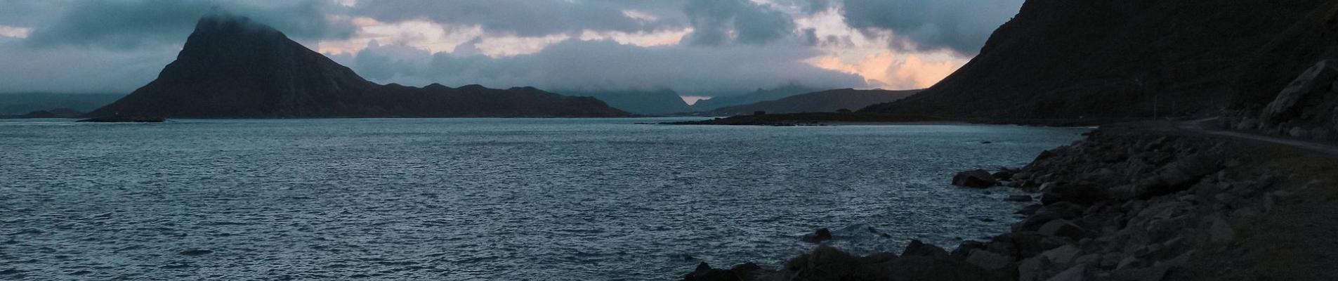 Picturesque scenery of rocky coast of rippling lake and silhouettes of rough mountains