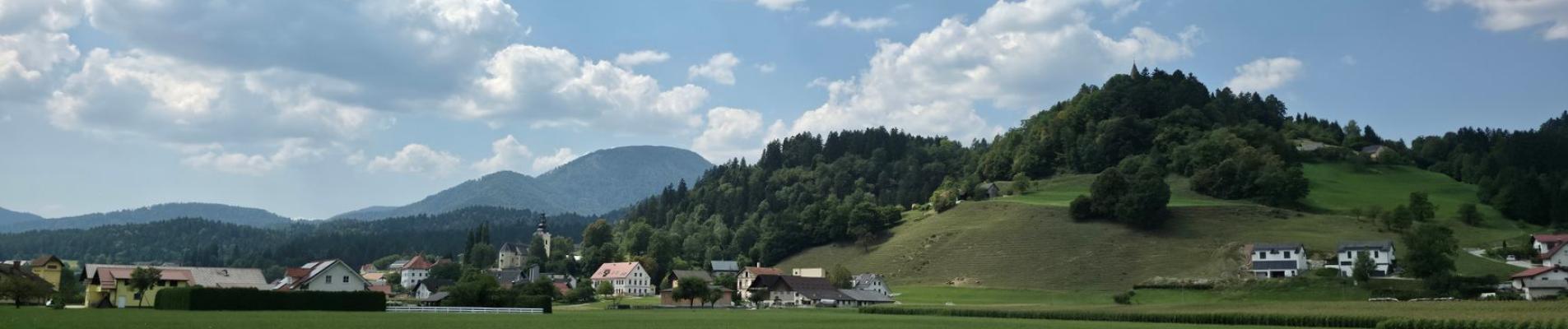 Peaceful rural landscape with rolling hills and small village under a blue sky in Slovenia.