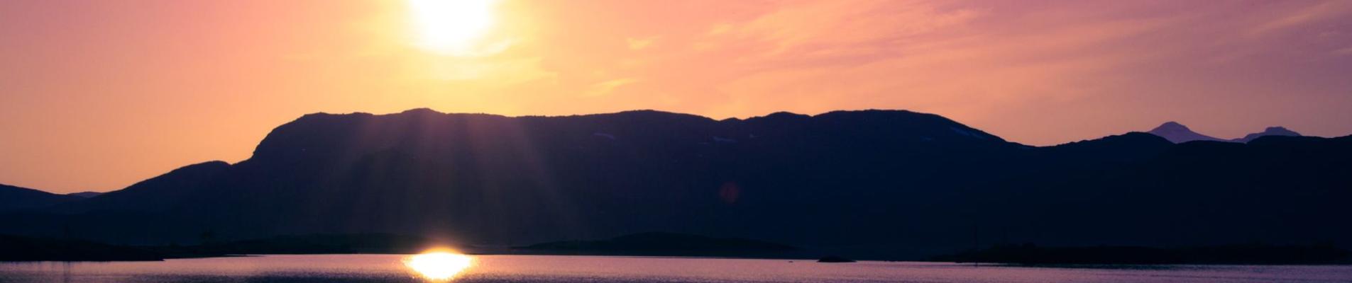 Stunning sunset over a tranquil lake with mountain reflections in Björkliden, Sweden.