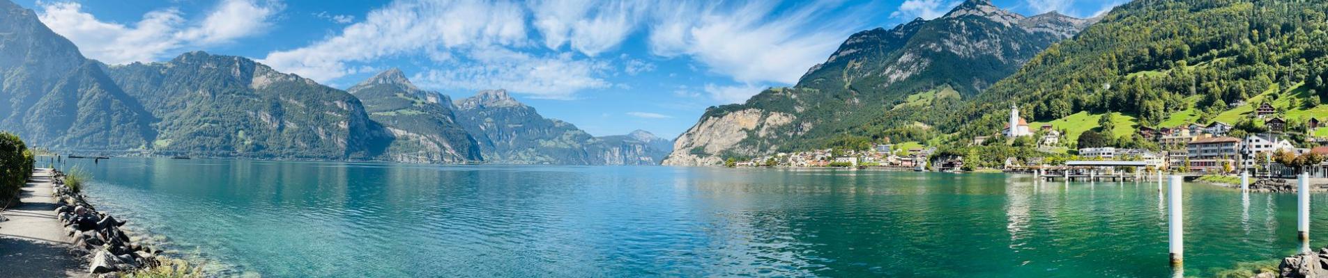 Stunning panoramic view of a lake with mountain backdrop under a bright sky in Flüelen, Switzerland.
