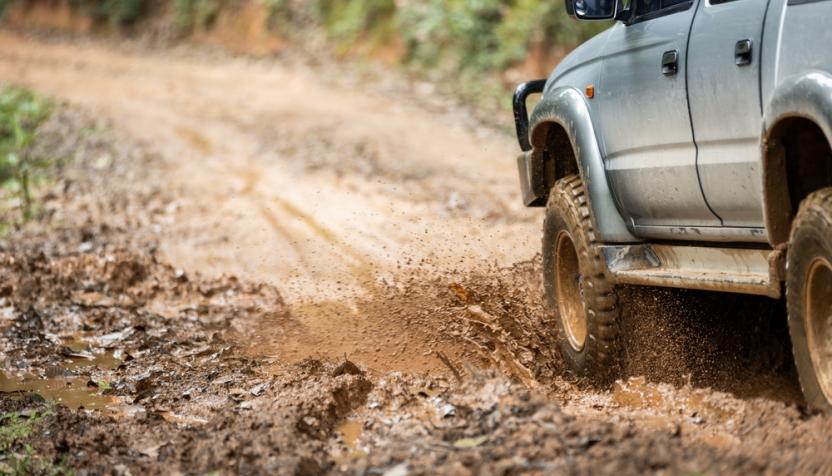 Ein Geländewagen fährt über eine schlammige Piste und wirbelt Matsch auf. Der Fokus liegt auf den Reifen und den spritzenden Schlammtropfen.