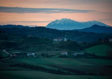 A tranquil rural scene in Albania, showcasing rolling hills and mountains under a sunset sky.