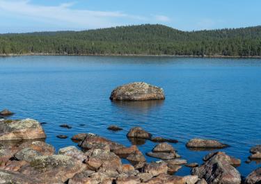 Tranquil lake scene with rocks and forested hills in Norway under a clear sky.