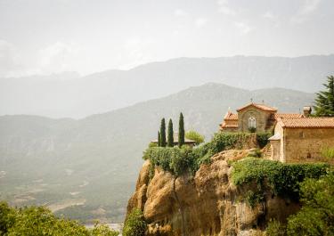 Picturesque monastery perched on a dramatic cliff with mountain backdrop.