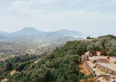 Breathtaking aerial view of Kerkyra's lush landscape with hills, valleys, and ancient structures under a clear sky.