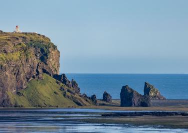 Breathtaking view of Icelandic coastline featuring a cliff, lighthouse, and ocean under clear skies.