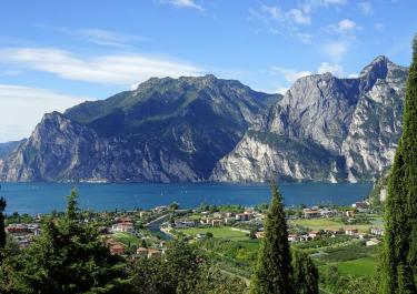 Scenic view of Lake Garda with surrounding mountains and lush green trees in the foreground.