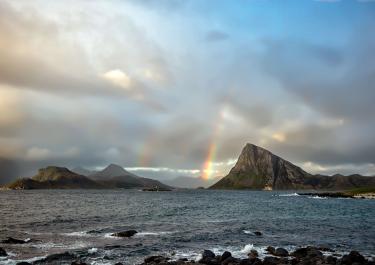 Scenic view of a rainbow arching over the rugged coastline of Offersøya, Nordland, Norway.
