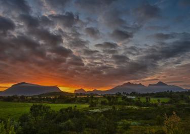 Breathtaking view of sunset over lush fields and distant mountains in Nordland, Norway.