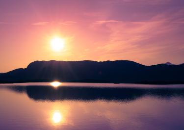 Stunning sunset over a tranquil lake with mountain reflections in Björkliden, Sweden.