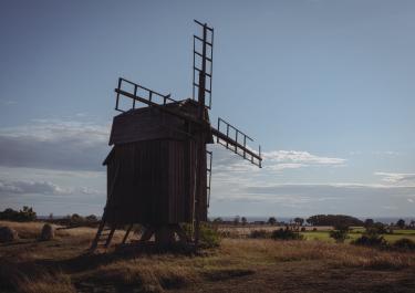 A traditional wooden windmill stands alone in the scenic Swedish countryside during a sunny day.