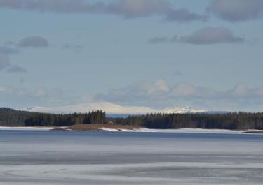 Serene winter landscape with snowy mountains, frozen lake, and blue sky in Sweden.