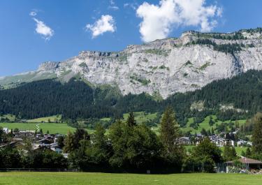 Stunning view of alpine village with majestic mountains and lush greenery under a bright blue sky.
